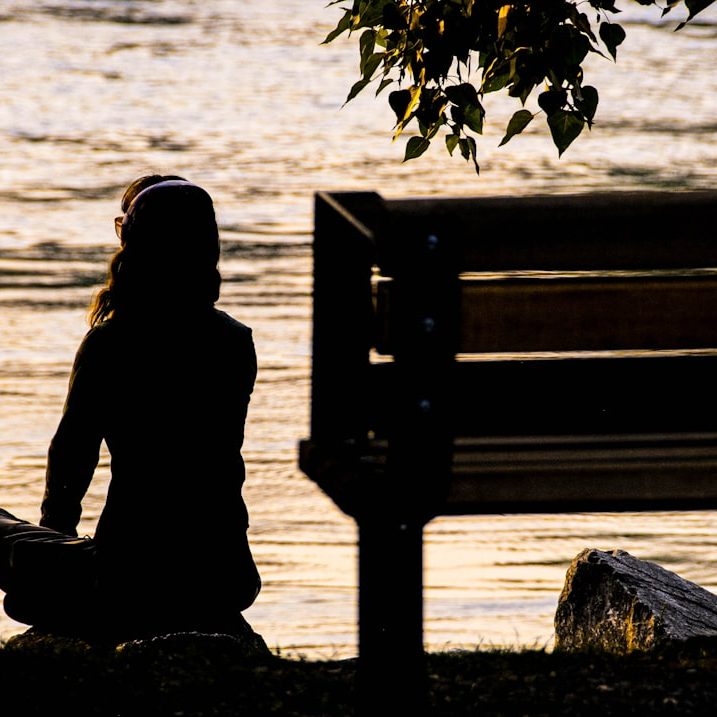 silhouette of person sitting on bench near body of water during daytime